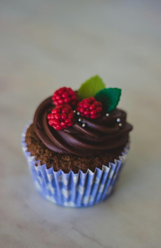 A delicious chocolate cupcake topped with berries and green leaves, perfect for desserts.