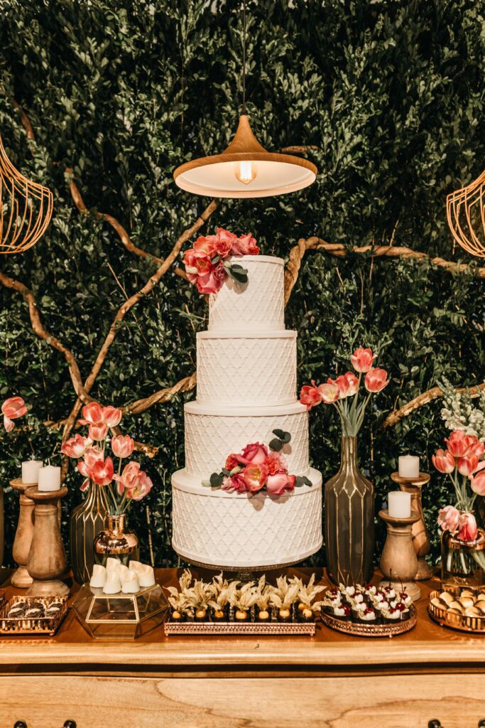 A beautifully decorated wedding table featuring a three-tiered cake, flowers, and desserts in a romantic setting.